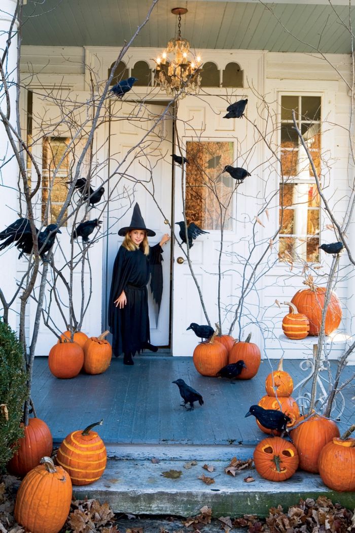 Decoração de Halloween, muitas abóboras e corvos, uma pequena bruxa na frente da porta, esculpir abóboras