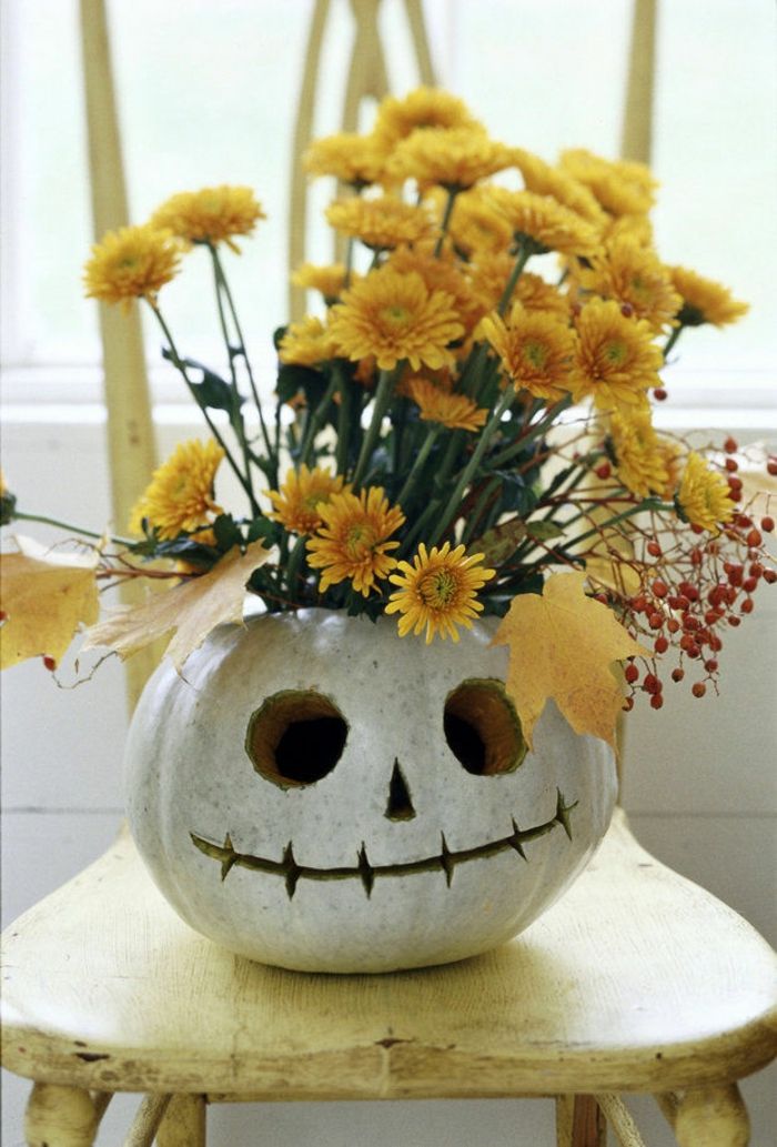 una faccia di zucca bianca con fiori gialli e foglie come decorazione