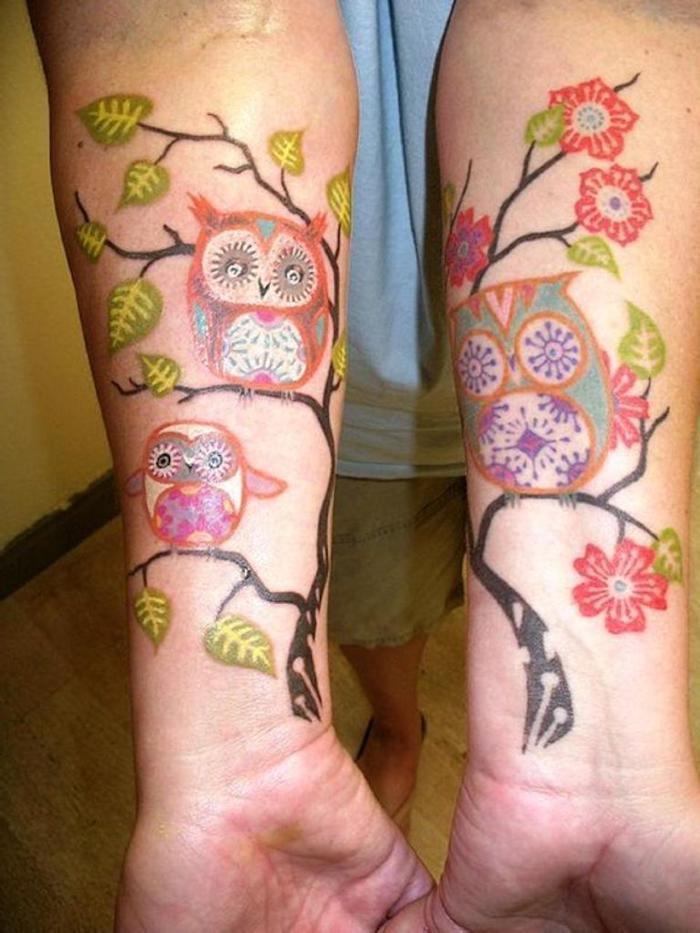 två händer med fantastiska färgglada tatueringar med ugglor och uhu och ett träd med gröna blad
