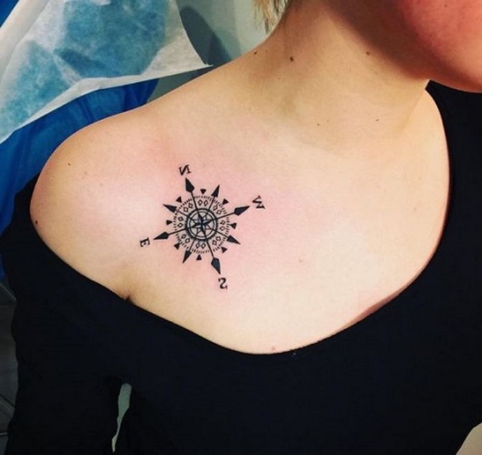 Tai maža juoda tatuiruotė su mažu juodu kompasu ant moters peties