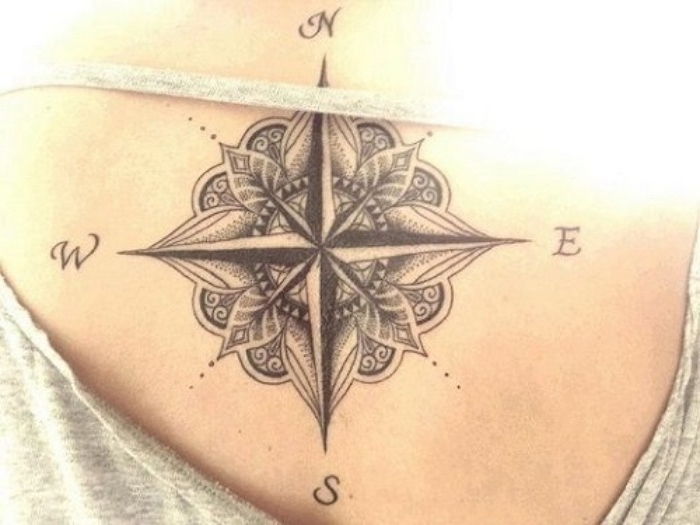 Juodas kompasas su mažais juodais lapais - tatuiruotė jaunos moters gale