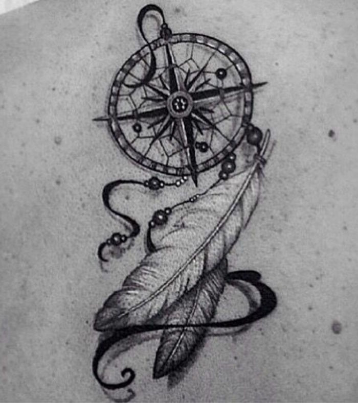 En svart tatuering med en liten svart kompass och två vackra vita långa fjädrar