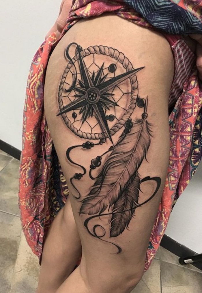 En stor tatuering med en stor svart kompass med svarta pilar och två långa vita fjädrar - idé för en tatuering för kvinna