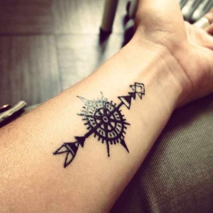 kompasstatuering - en hand med en svart tatuering med en svart lång pil och en liten svart kompass - tatuering på handleden