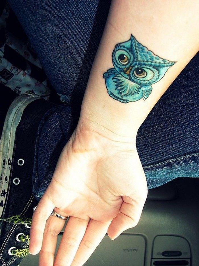 En hand med en owltatuering på handleden - blå liten uggla med gula ögon