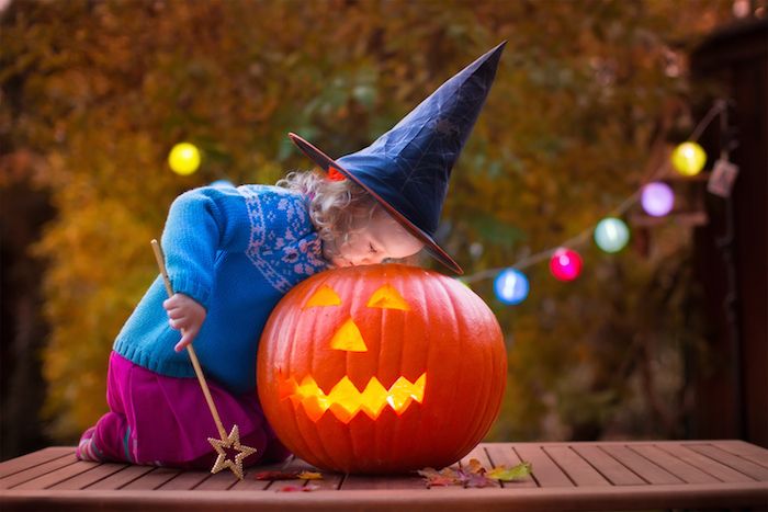 una bambina vestita da strega gioca con la faccia di zucca su Halloween