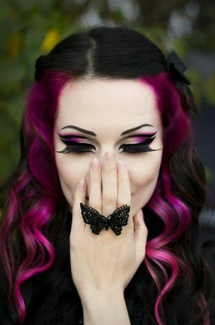 Gotiska look - svart hår med lila sido trådar med stora lockar, stark violett-vit makeup - ögonskugga i två färger, svart eyeliner och stora lösögonfransar, sidofingrar fastnat hiinten med två svarta hårspännen, svart ring i form av en fjäril