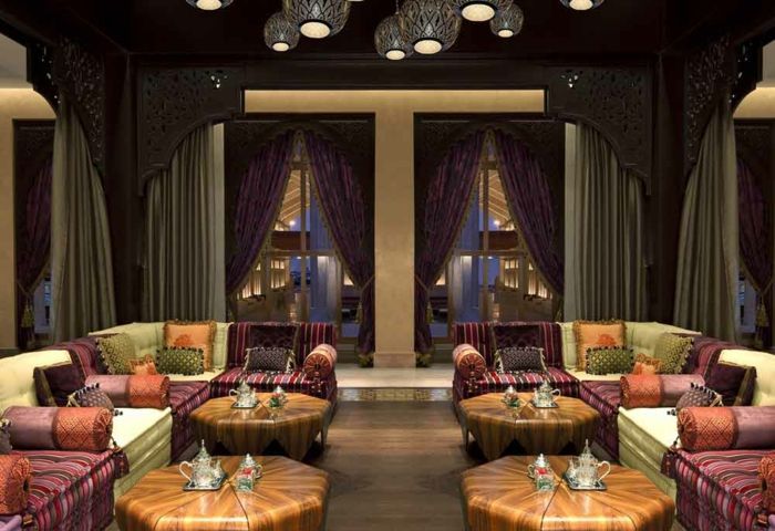 Cafe v Maroku s štirimi lesene mize z okrogle oblike, udobno Eckcouchen s pisanimi tkaninami, majhnem trgu in okrogle blazine, težke zavese, ki se uvrščajo v sivi in ​​vijolični, okrogle oblikovalec luči, strop z okraski