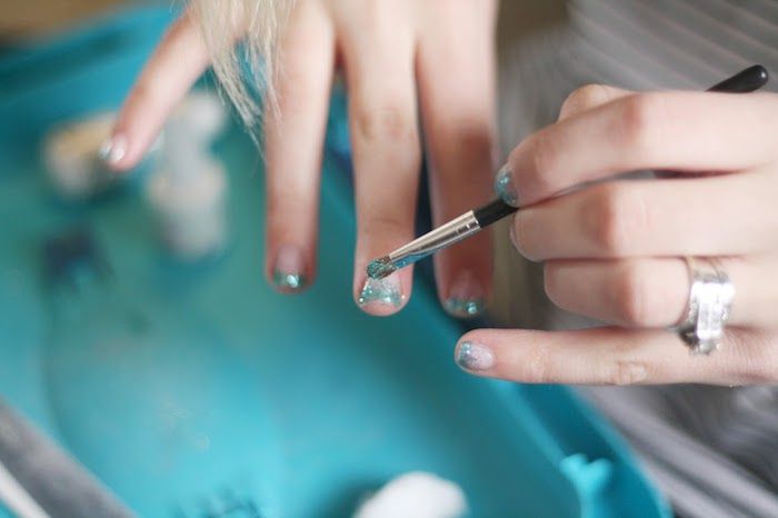 Applicare le unghie in gel glitterate sulle unghie e tamponare i disegni brillanti delle unghie in blu