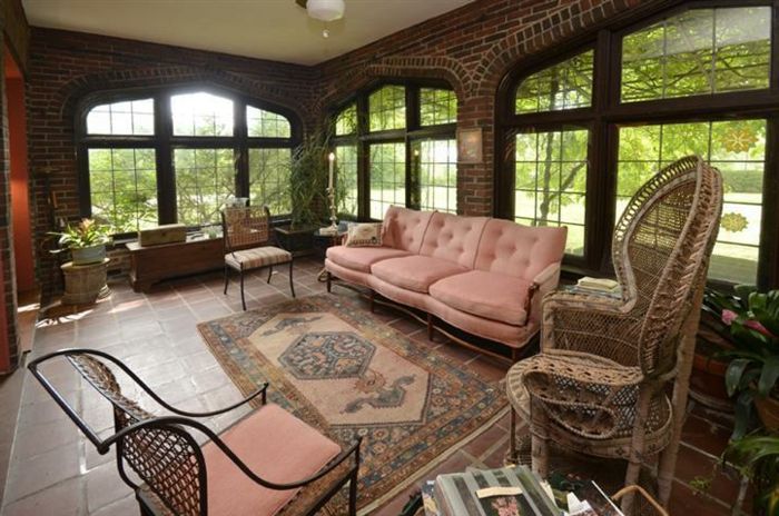 Soba z orientalskim pohištvom v naravnih barvah, pepelnik roza kavč z nasloni za roke, preproga v zemeljskih tonih, hiša z opečnimi stenami, velika velika okna