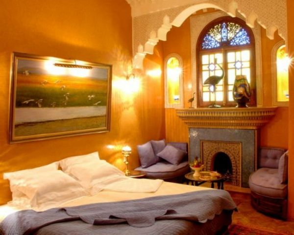luksuzni kamin in oranžne barvne sheme v elegantni orientalski spalnici