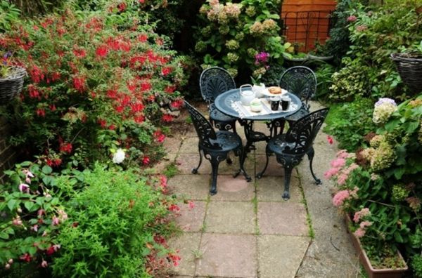 grădină frumoasă, cu multe flori colorate și o mică masă de cafea cu patru scaune