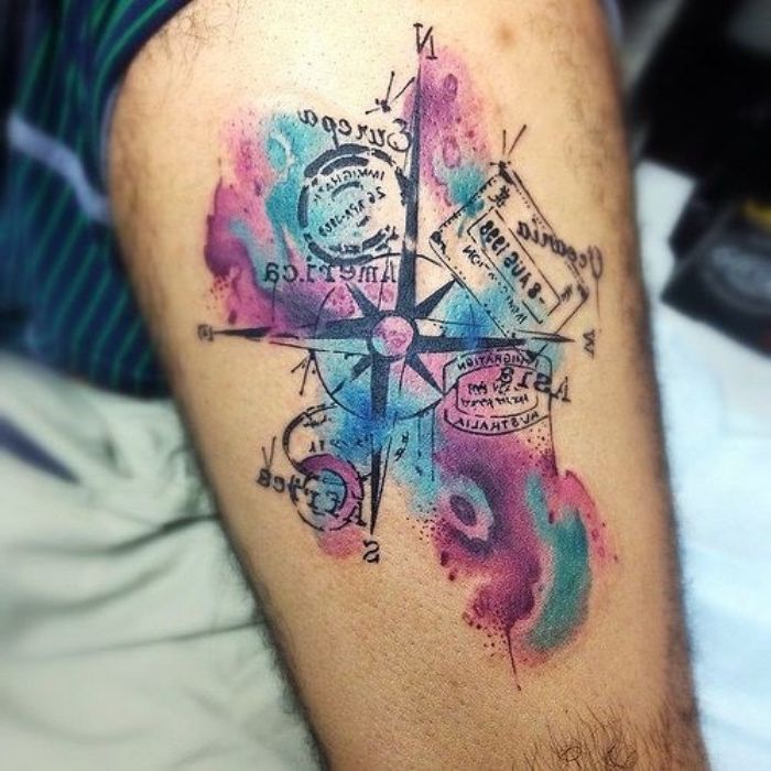 En stor tatuering med en stor svart kompass med svarta pilar och frimärken och färgglada färger på handen