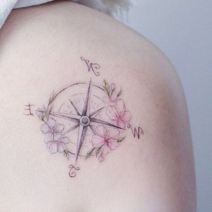 en veldig fin tatovering med små rosa og lilla blomster og et kompass på ryggen