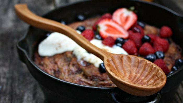 Venda de bordados, um pote de cerâmica preta com bolo e frutas vermelhas frescas, creme, colher de pau