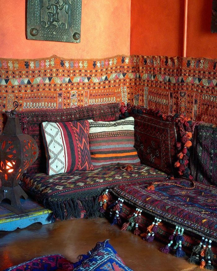 Kavč v temnih barvah, pokrov kavčev z rešetkami, oranžno poslikana stena z kovinskim dekoracijskim zidom, kovinska talna svetilka z vreteno