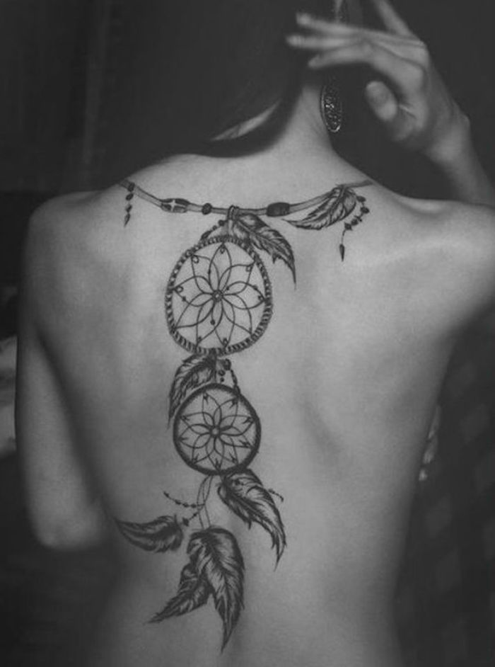 Tatuagem de apanhador de sonhos nas costas de uma mulher com grandes brincos