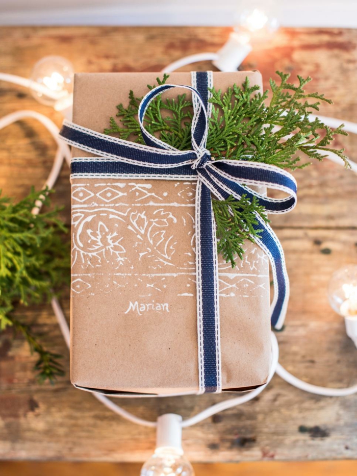 Kreativ emballasje av gaver - brunt papir, blått bånd og kvist, trykt navn