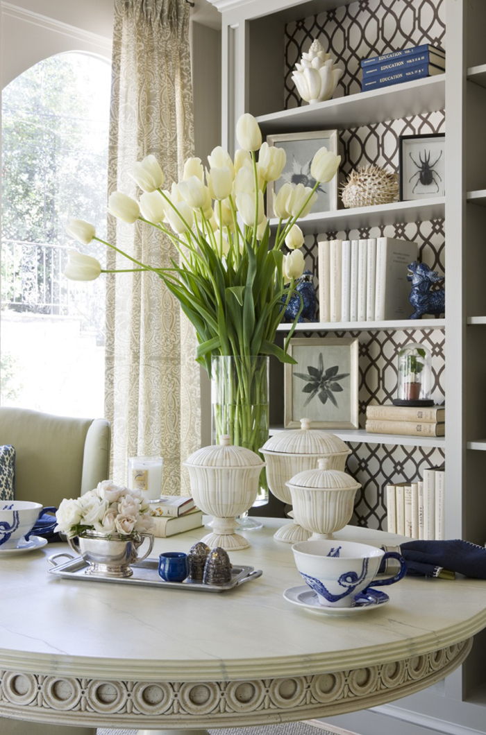 Salotto vintage, tavolo in legno, bouquet di tulipani, porcellane, scaffali con libri e foto su di esso