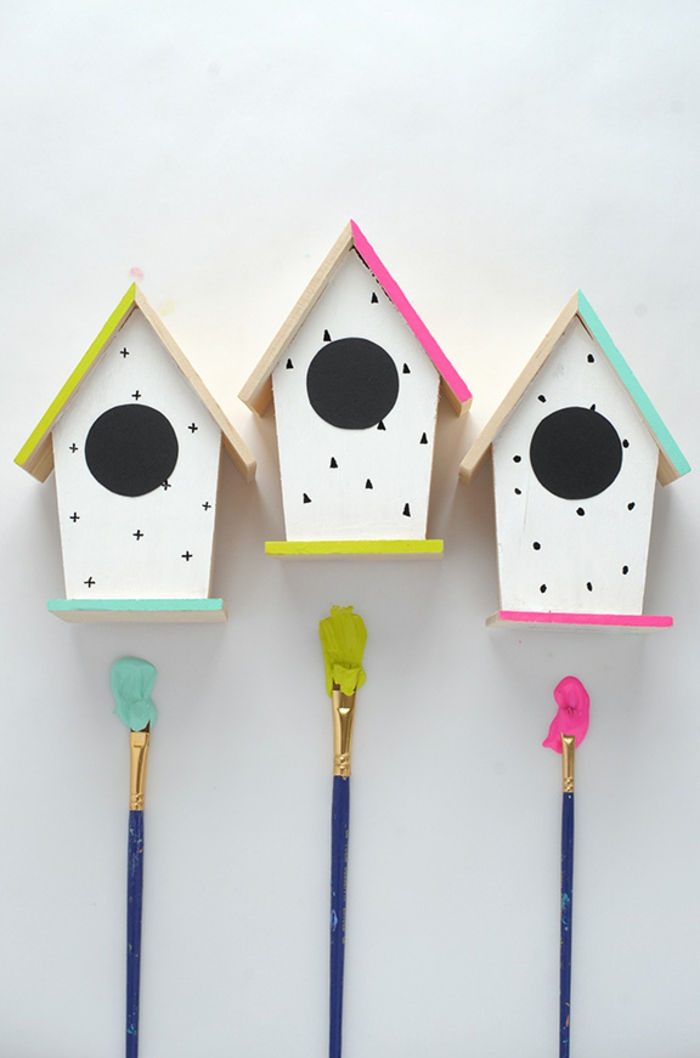 Tre fuglkasser laget av tre, hvite vegger dekorert med prikker, kryss og trekanter, fargerike tak