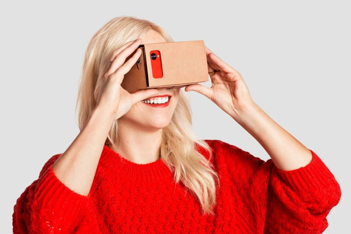 Tukaj je nasmejana ženska z lepim rdečim puloverjem - VR očala iz kartona in rdečim mobilnim telefonom
