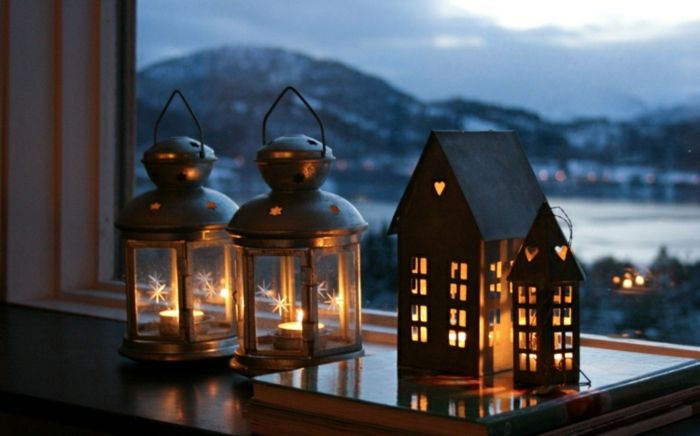Dekorasjon for helgenbøye - Hus laget av kartongbelysning inne, hull i form av hjerter, to lanterner laget av glass og metall, en haug med store bøker, vinduer med utsikt mot fjellene, snø i fjellet