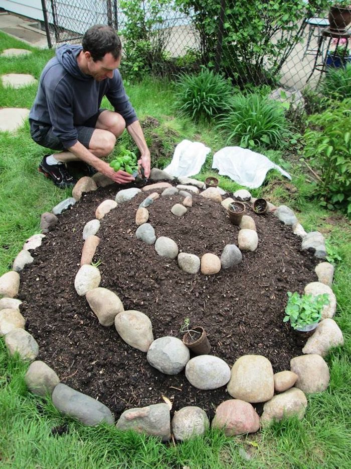 Nå viser vi dem en god idé på temaet hage design som kan appellere til dem veldig godt - et inspirerende bilde med en mann og en liten mini urt spiral med grønne planter og små steiner