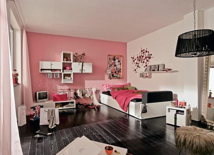 rumsmöbler idé svart trägolv rosa väggar med dekoration i vita hyllor med böcker och inredning liten tv-sänglampa