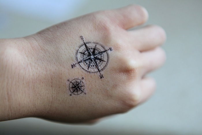 To vakre små kompass tatoveringer med svarte kompasser på hånden